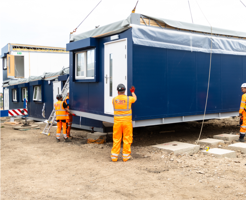 a modular building is lowered onto prepared groundworks by a team
